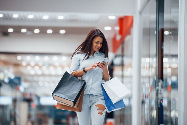 
                        Lächelnde Frau spaziert mit Einkaufstauschen durch ein Shopping-Center
                                              
